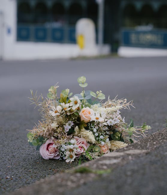 A delicate bouquet of fresh flowers resting on the pavement next to a curb, featuring soft pink roses, white daisies, and small white filler flowers, accented with light green eucalyptus leaves and wi